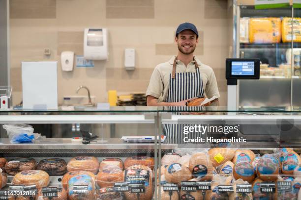 portret van de jonge verkoper staande achter de toonbank van de delicatessen sectie geconfronteerd met camera erg blij - delicatessenzaak stockfoto's en -beelden