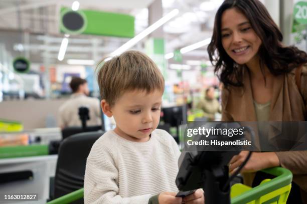 schattige baby jongen introductie kaart op creditcard lezer bij het afrekenen van de supermarkt, terwijl mam toezicht houdt zeer vrolijk - supermarket register stockfoto's en -beelden