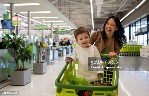 美麗的母親推車與她的幼兒裡面與購買雜貨離開超市,面對相機微笑 - 大賣場 個照片及圖片檔