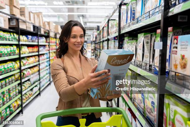 mooie jonge vrouw kiezen een graansoort van plank winkelen voor boodschappen in de supermarkt - cereal box stockfoto's en -beelden