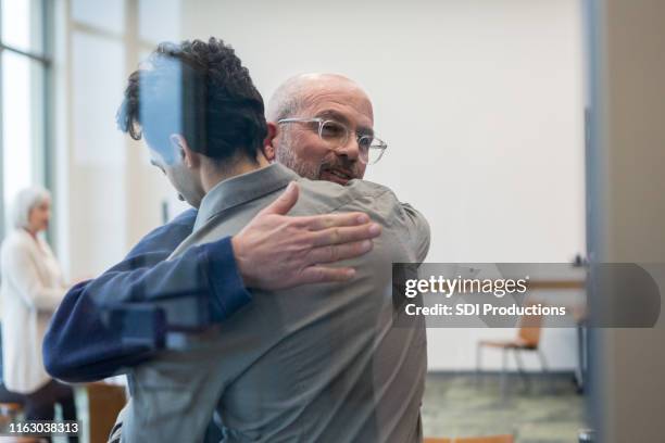 mature adult father and mid adult son share a hug - family therapy stock pictures, royalty-free photos & images