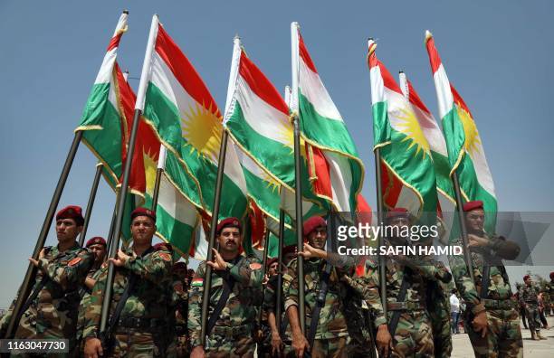 Members of the Iraqi Kurdish Peshmerga stand holding flags of Iraq's autonomous Kurdistan region a training session by German military officers...