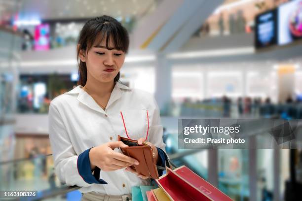portrait of unhappy stressed beautiful person looking in open wallet with shocked expression while holding color shopping bags at mall. young model spent too much money during shopping time - luxury girl imagens e fotografias de stock