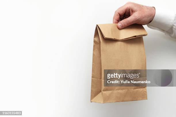 close up male holds in hand clear empty blank craft paper bag for takeaway isolated on white background. packaging template mock up. delivery service concept. copy space. - lunch bag white background stock pictures, royalty-free photos & images