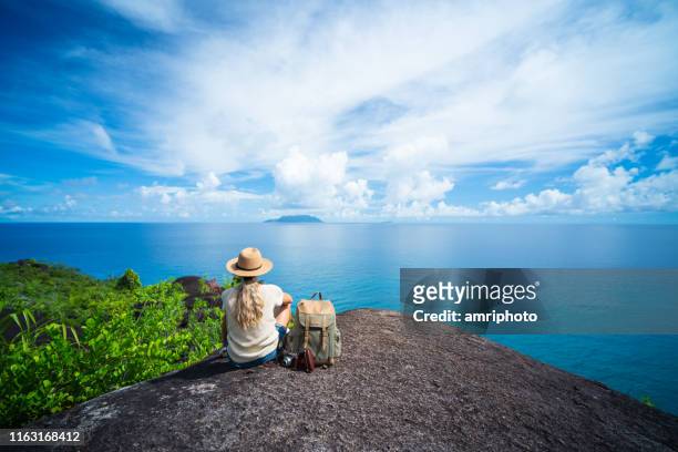 solo-reisende zurück blick auf eine frau sitzt auf felsen der tropischen insel genießen meerblick - seychellen stock-fotos und bilder