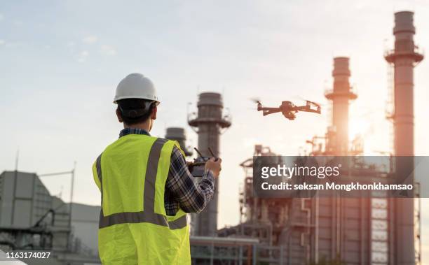 asian construction worker piloting drone at building site. video surveillance or industrial inspection - drohnen stock-fotos und bilder
