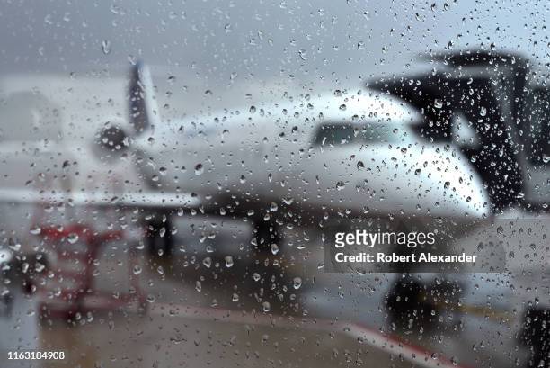 Rain-covered window obscures the view through a terminal window of an United Express passenger plane at a gate at Denver International Airport in...