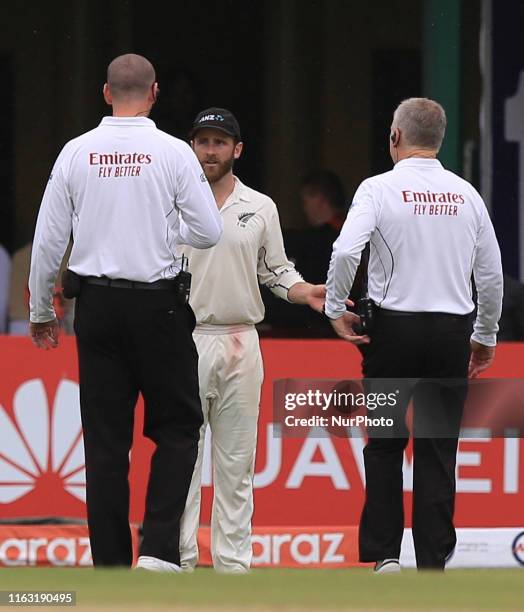 New Zealand cricket captain Kane Williamson talks with on field umpires Michael Gough and Bruce Oxenford as ground staff cover the ground while rain...