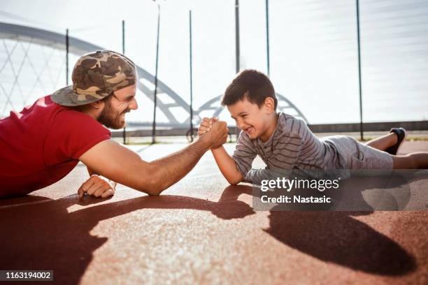 father and son having fun with arm wrestling on a sports court - arm wrestle stock pictures, royalty-free photos & images