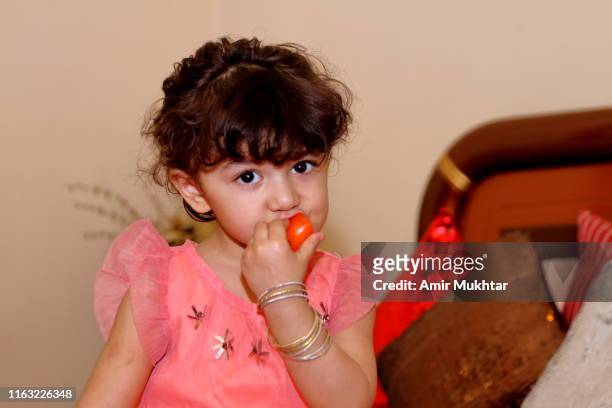 a young cute girl eating tomato fruit and looking at the camera - punjabi girls images 個照片及圖片檔