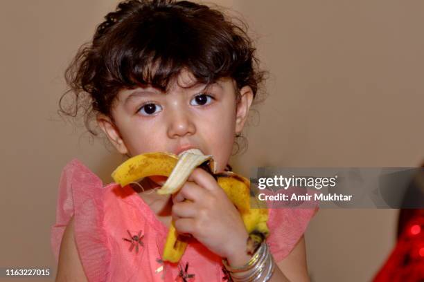 a young cute girl eating banana fruit and looking at the camera - punjabi girls images 個照片及圖片檔