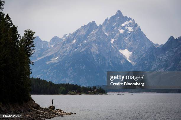 Tourist stands on a rock along the shore of Jackson Lake in Jackson Hole, Wyoming, U.S., on Thursday, Aug. 22, 2019. Over the past two decades,...