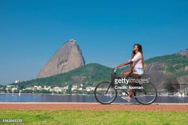 femme conduisant un vélo devant le pain de sucre - rio de janeiro photos et images de collection
