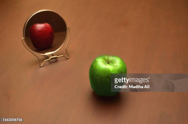 a green apple seeing its real reflection in mirror red, thereby depicting true reflection is usually different from whats on the face. - truth lies 個照片及圖片檔