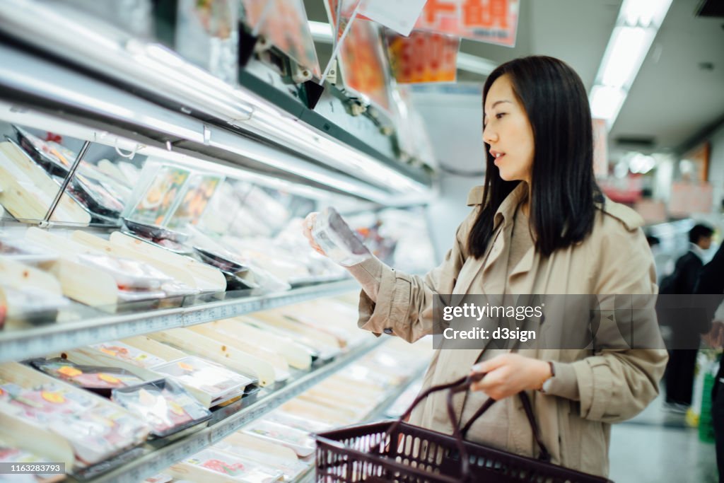 Young Asian woman grocery shopping and choosing fresh poultry in supermarket