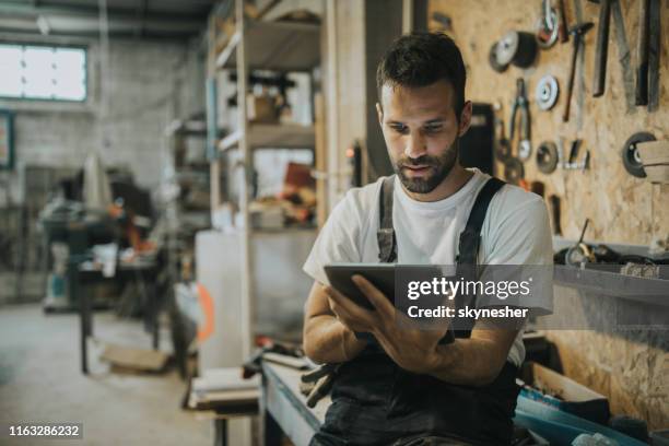 young manual worker using digital tablet in a workshop. - reading digital tablet stock pictures, royalty-free photos & images