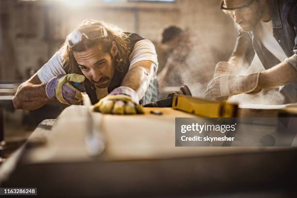 junge arbeiter messen stück holz während der arbeit mit kollegen in der schreinerei. - präzision stock-fotos und bilder