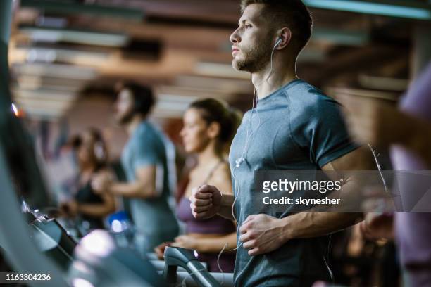 athletic man listening music while running on treadmill in a gym. - health club stock pictures, royalty-free photos & images