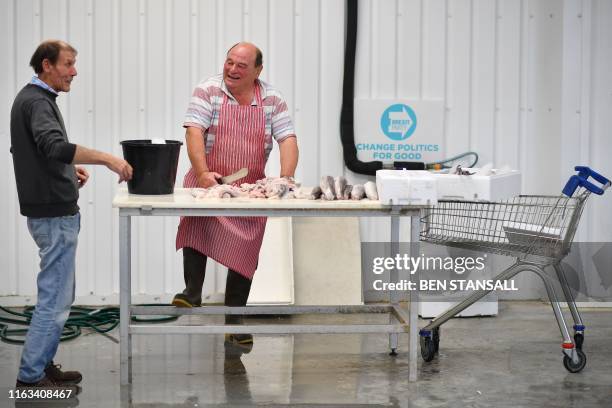 Fishmonger Lenny Walters shares a joke with a colleague as he prepares hake in Milford Haven in Wales on August 21, 2019. - Locals in Milford Haven...