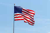 American flag waving on pole with bright vibrant red white and blue colors against blue sky