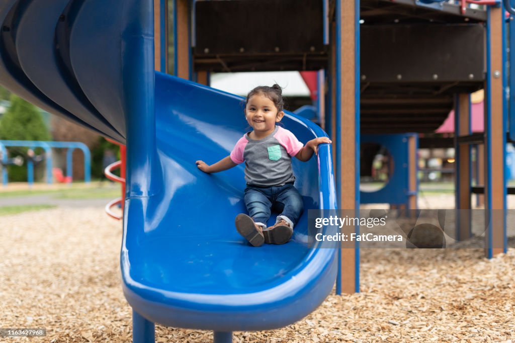 A toddler-age girl riding down the slide
