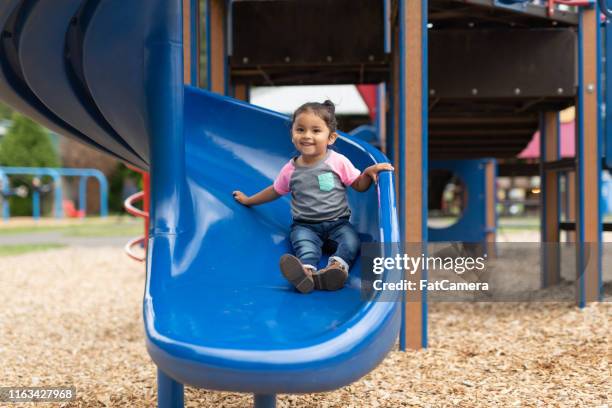 a toddler-age girl riding down the slide - children's slide stock pictures, royalty-free photos & images