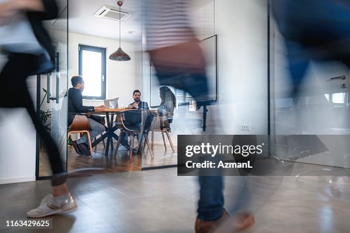 Businesspeople in Conference Room and Colleagues Walking By Businesspeople in Conference Room and Colleagues Walking By