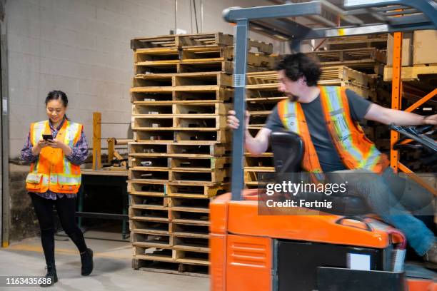 an industrial warehouse workplace safety topic. a female worker distracted by her mobile cell phone as a forklift approaches. - workplace danger stock pictures, royalty-free photos & images