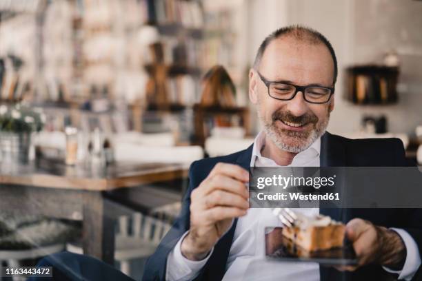 mature businessman having a piece of cake on a digital tablet in a cafe - eating cake stock-fotos und bilder