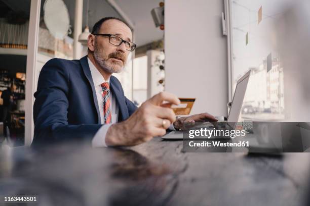 mature businessman using laptop and credit card in a cafe - bankschalter stock-fotos und bilder