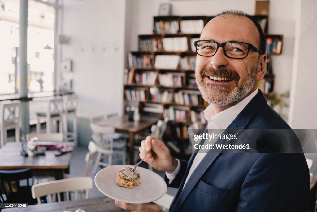 Smiling mature businessman having a piece of cake in a cafe
