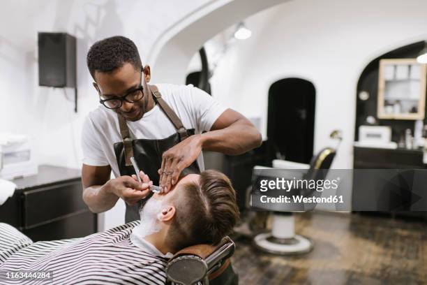 man getting his beard shaved with razor in barber shop - straight razor stock pictures, royalty-free photos & images