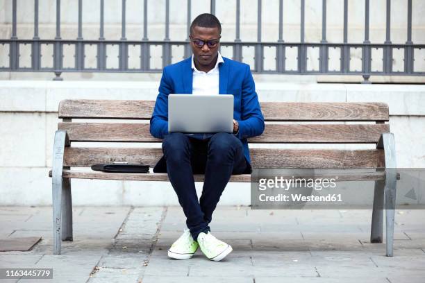 young businessman wearing blue suit jacket sitting on bench and using laptop - businessman in suit ストックフォトと画像