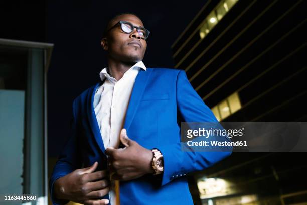 young businessman wearing blue suit jacket, ooking sideways at night - elegante kleidung stock-fotos und bilder