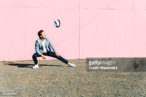 young man in front of pink construction barrier, watching his hat flying in the wind - pink hat - fotografias e filmes do acervo
