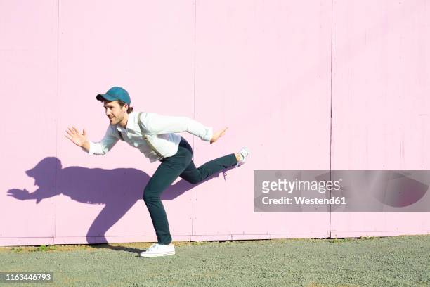 young man in front of pink construction barrier, balancing on one leg - mime stockfoto's en -beelden