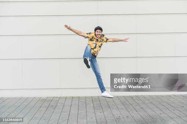 young man wearing flat hat and aloha shirt, jumping for joy - flat cap stock-fotos und bilder