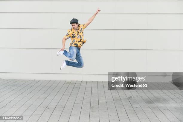 young man wearing flat hat and aloha shirt, jumping for joy - flat cap stock-fotos und bilder