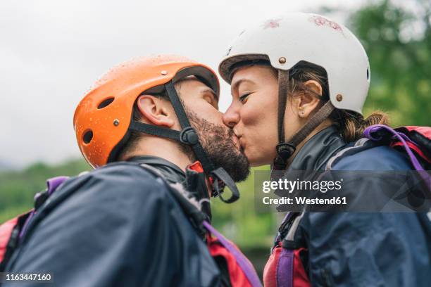 couple wearing safety helmets kissing outdoors - sport schutz stock-fotos und bilder