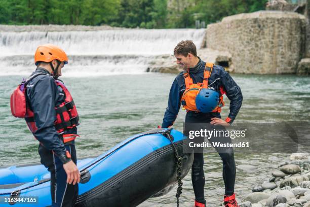 two men with rubber dinghy at river shore - rubber raft stock pictures, royalty-free photos & images