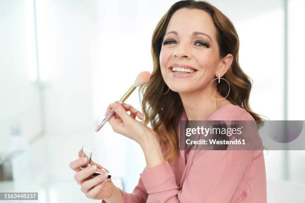 portrait of happy woman applying make up at home - blush makeup ストックフ��ォトと画像