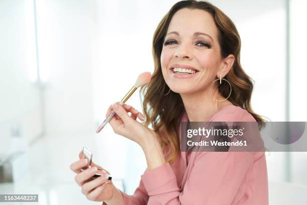 portrait of happy woman applying make up at home - woman applying blush stock pictures, royalty-free photos & images