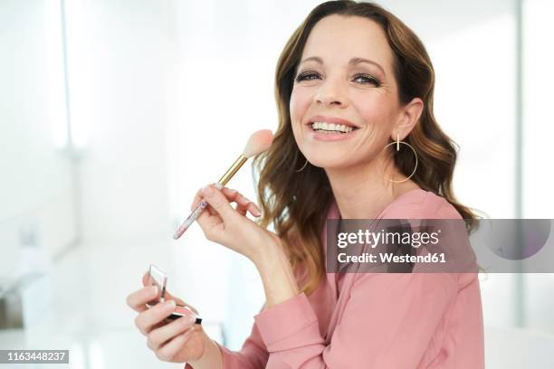 portrait of happy woman applying make up at home - make up blush imagens e fotografias de stock