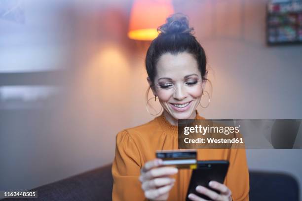 smiling woman using smartphone and credit card at home - red blouse fotografías e imágenes de stock