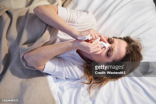 woman lying in bed blowing her nose - virus grippe stock pictures, royalty-free photos & images