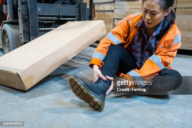 an industrial warehouse workplace safety topic.  a female employee injured by tripping over forklift forks. - tropeçar imagens e fotografias de stock