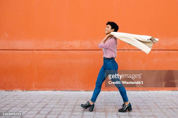 businesswoman walking at a red wall in the background, putting her jacket on her shoulder - zelfvertrouwen stockfoto's en -beelden