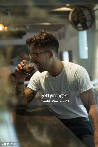 laughing young man having a drink at the counter of a bar - bar man t shirt ストックフォトと画像