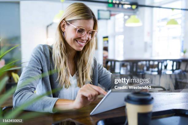 young woman using her digital tablet while drinking coffee in the coffee shop - looking at ipad fotografías e imágenes de stock