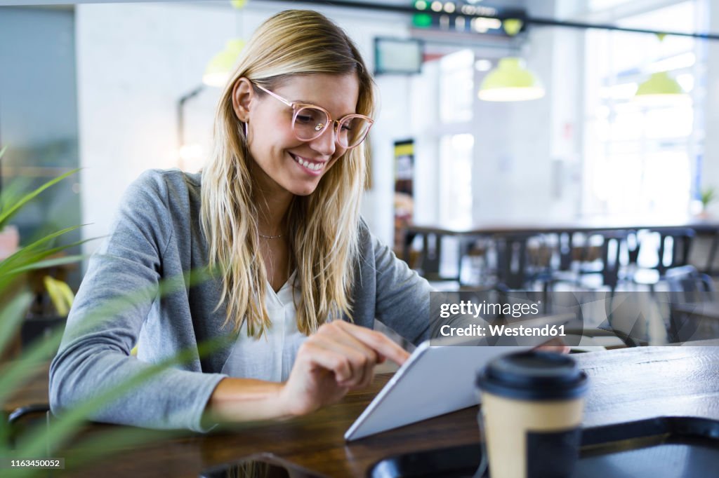 Young woman using her digital tablet while drinking coffee in the coffee shop